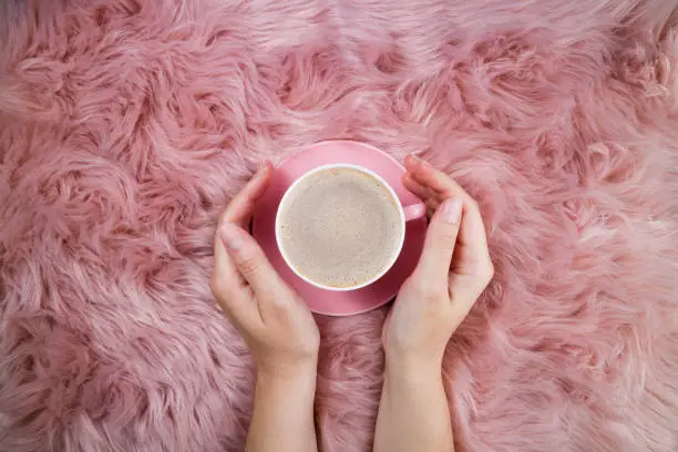Photo of Female hands and coffee cup on pink woolen fur. Femininity trendy background. Morning coffee, breakfast, weekend