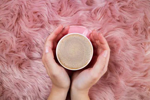 Photo of Female hands and coffee cup on pink woolen fur. Femininity trendy background. Morning coffee, breakfast, weekend