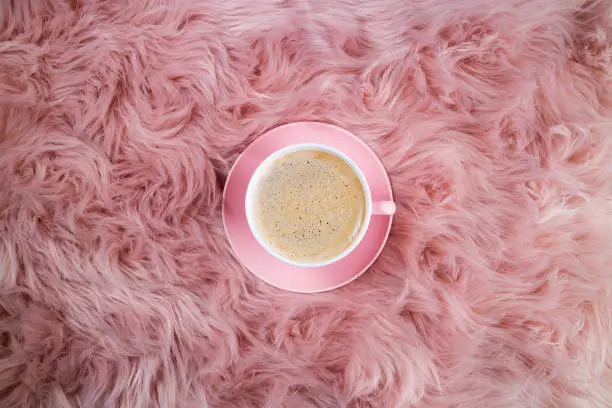Photo of Coffee cup on pink woolen fur. Female trendy background. Breakfast, domestic life, weekend, hygge and cozy atmosphere