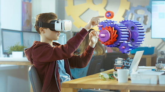 En un muchacho de clase de ciencia de computadora uso de casco de realidad Virtual trabaja en entorno 3D interactivo. Proyecto de modelado mecánico de engranajes de conexión con el Software de realidad aumentada. photo
