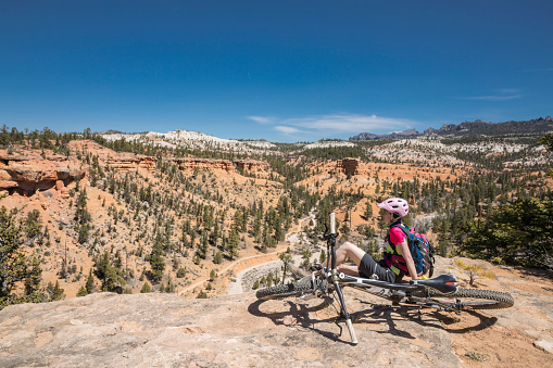 A female mountainbiker is taking a break at a viewpiont at Casto Canyon nearby Red Canyon which is located in southwestern Utah nearby Bryce Canyon within the Dixie National Forset. The red, orange, and white colors of the rocks provide spectacular views for park visitors.\nCanon EOS 5D Mark IV, 1/125, f/18, 24 mm.