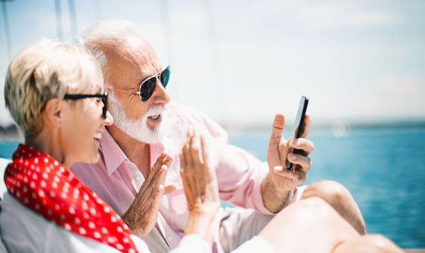 We are having so much fun on the cruse. Senior couple on the sailing boat cruise video calling to their grandchildren. They are waving at them and teling them how much they enjoying summer vacation. yacht selfie stock pictures, royalty-free photos & images
