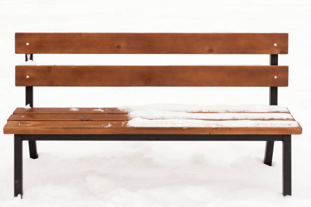 The cold seat, wooden bench covered in a thick layer of snow, with icicles hanging down on a snowy winters day.
