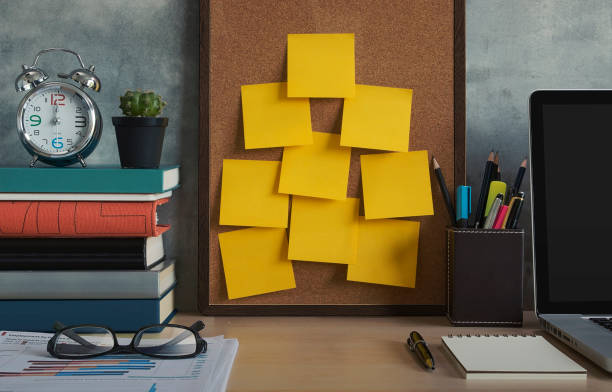 risoluzioni, note, obiettivi, post, memo o concetto di piano d'azione. note adesive sulla tavola di sughero nell'ufficio del posto di lavoro con laptop, notebook, occhiali da vista, orologio, pianta, libri e articoli di cancelleria su scrivania di legno. - bulletin board office note pad wood foto e immagini stock