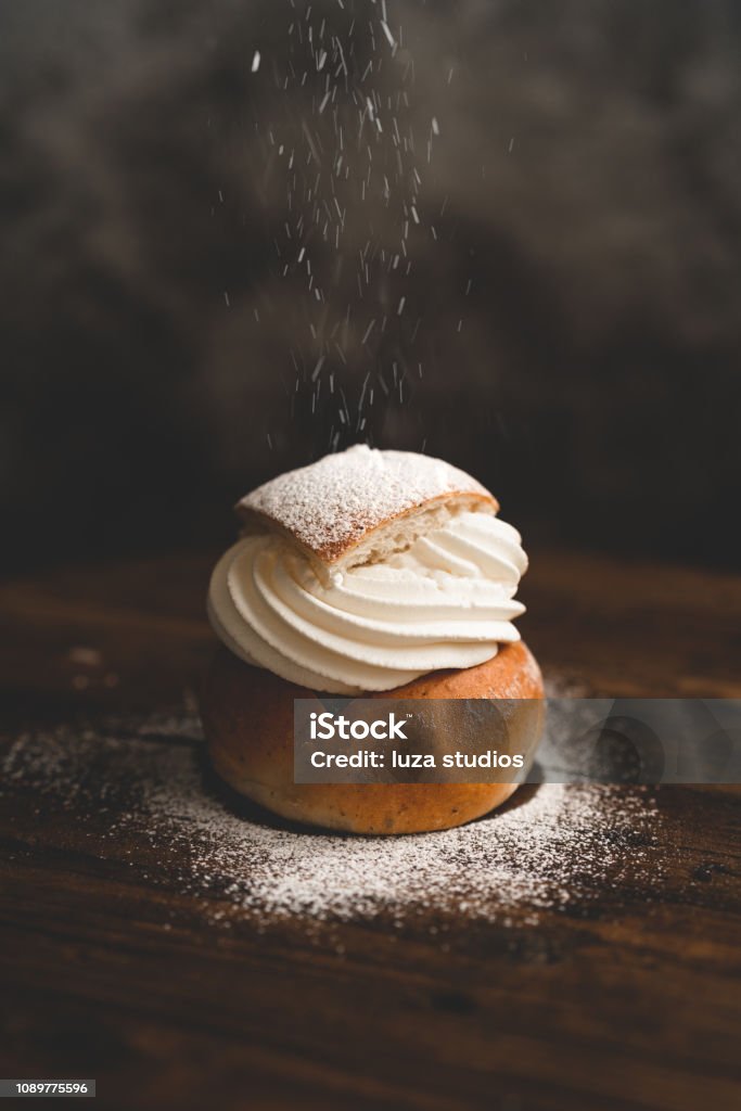 Traditional Swedish dessert Semla with whipped cream and sugar Sprinkling powdered sugar on a traditional Swedish dessert called semlor. Cake Stock Photo