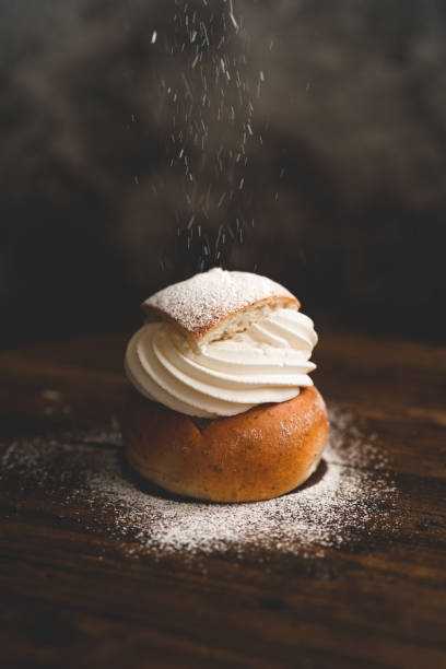Traditional Swedish dessert Semla with whipped cream and sugar Sprinkling powdered sugar on a traditional Swedish dessert called semlor. baked pastry item stock pictures, royalty-free photos & images