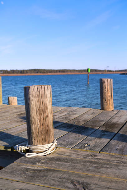 Boat Pier Closeup with bay and channel marker in background Boat Pier Closeup with bay and channel marker in background. The old wooden pier is taken in winter with a clear sky. The water is blue and you can see a green channel marker in the background with marshland on the other side of the water in the bay. There is a rope tied around one of the pylons. The dock photo is taken in coastal Virginia in the Chesapeake bay area. A nice nautical waters edge landscape nature take in the outdoors. channel marker stock pictures, royalty-free photos & images