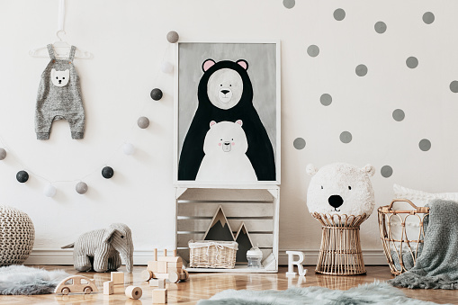 Stylish scandinavian kid room with mock up photo poster frame on the pattern wall, boxes, teddy bear and toys. Cute modern interior of playroom with white walls, wooden accessories and colorful toys.