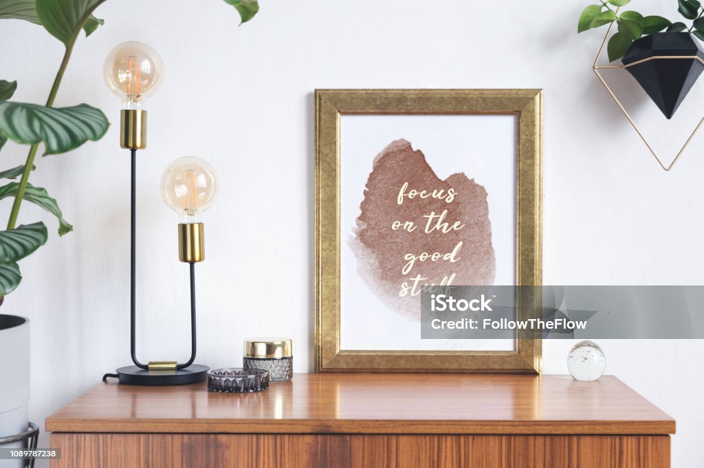 Retro and minimalistic white interior with gold mock up photo frame on the vintage brown shelf,t ropical plant in cement pot, table lamp and accessories. Concept of shelfie. Retro and minimalistic interior with mock-up photo frame on the vintage brown shelf. Animal Shell Stock Photo