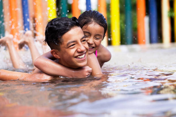 Latino children a teenage boy and an 8-year-old girl play in the pool, cuddle and cuddle in the water while smiling and having fun