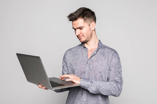 istock Confident young handsome man holding laptop and smiling while standing against white background 1089793414