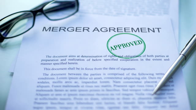 Merger agreement approved, officials hand stamping seal on business document