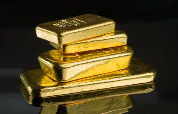 Several gold bars of different weight on a dark mirror surface.