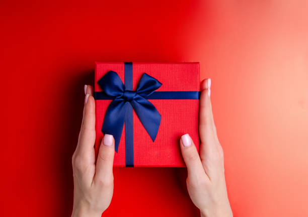 istock Red box gift with blue ribbon in hand on red background, top view 1089813854