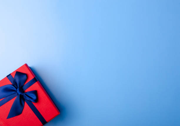 istock Red box gift with blue ribbon in hand on blue background 1089814244