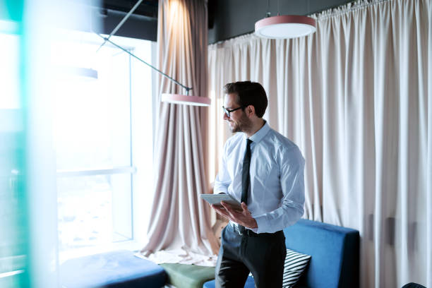 istock Smiling businessman in formal wear looking away and using tablet while standing in the office. 1089839722