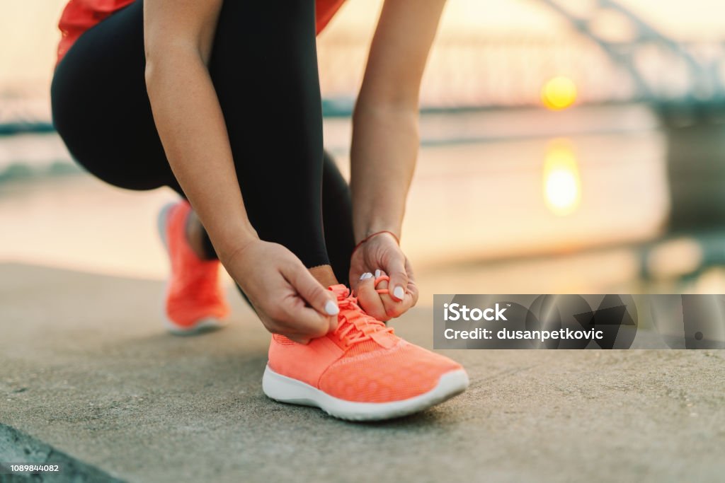 Gros plan de femme sportive tying shoelace agenouillés en plein air, au pont de fond. Concept de remise en forme de plein air. - Photo de Paire de baskets libre de droits