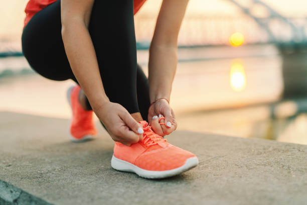 primo piano di donna sportiva legare laccio delle scarpe mentre in ginocchio all'aperto, in ponte di sfondo. concetto di fitness all'aperto. - sport running exercising jogging foto e immagini stock