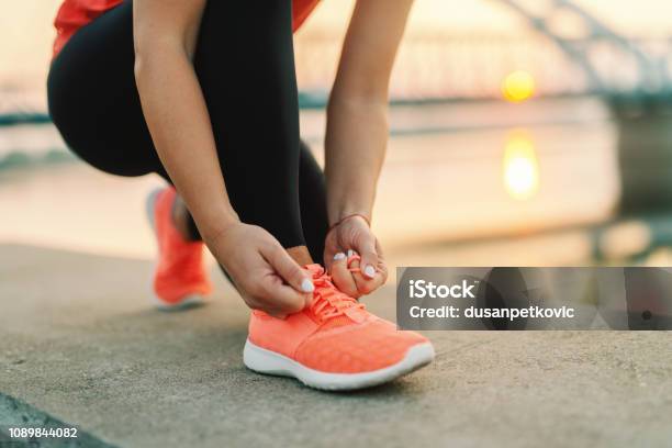 Foto de Feche De Mulher Desportiva Amarrando O Cadarço Enquanto Ajoelhandose Ao Ar Livre Na Ponte De Fundo Conceito De Fitness Ao Ar Livre e mais fotos de stock de Tênis - Calçados Esportivos