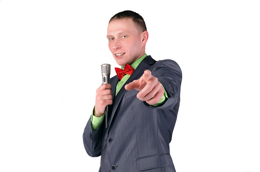 Happy presenter or businessman with microphone in the hands is showing ahead by his index finger isolated on white background.