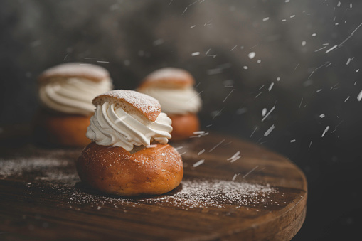 Sprinkling powdered sugar on a traditional Swedish dessert called semlor. The sugar is falling on the semlor like snow.