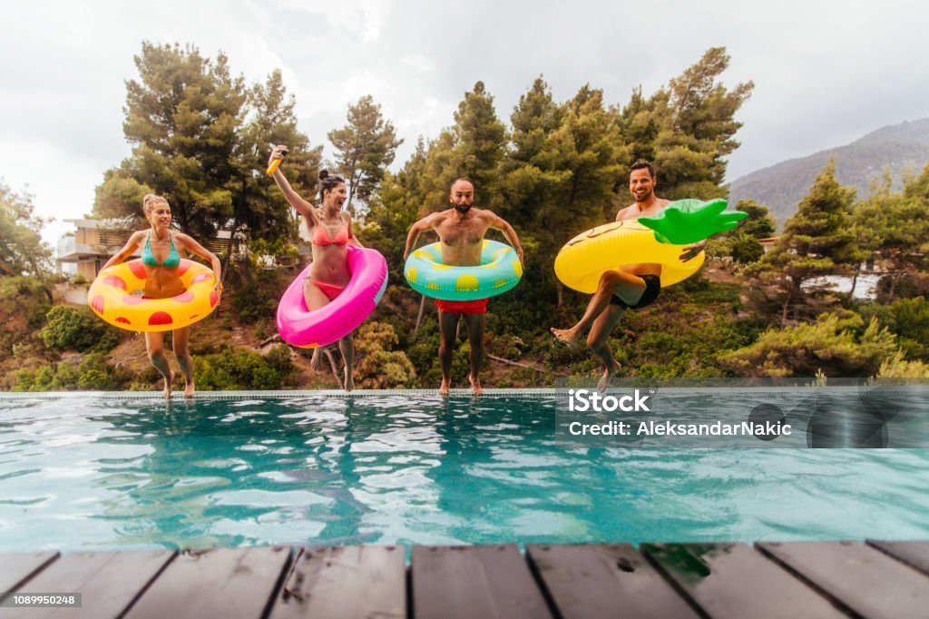 Friends are jumping into the pool Friends with inflatable rings jumping in the swimming pool Swimming Pool Stock Photo