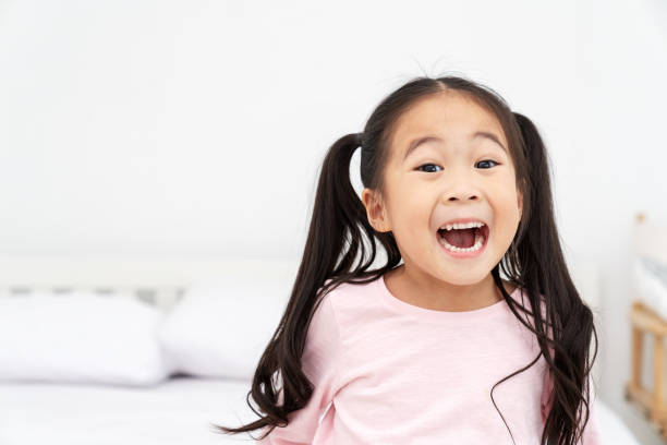 jovem bonita asiática menina sorrindo e rindo divertido sentir excitada, sorte e desfrutar weeken no fundo do quarto branco com close-up vista headshot. crianças pré-escolares de ásia ou conceito elementar de crianças. - child excitement awe fun - fotografias e filmes do acervo