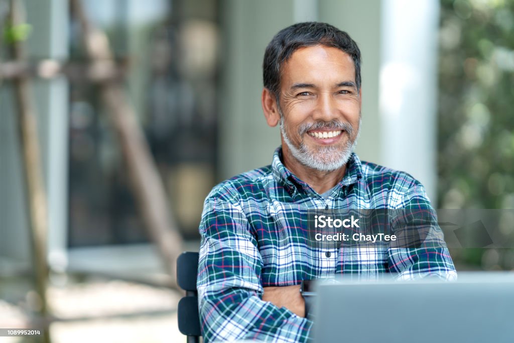 Retrato de homem maduro feliz com branco, cinza barba curta elegante olhando para a câmera ao ar livre. Lifestyle casual de reformados hispânico ou asiático adulto sorrir com confiante no café café. - Foto de stock de Homens royalty-free