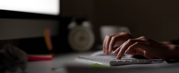 mano adicto al trabajo mecanografía teclado en oscura noche con luz de pantalla de ordenador, reloj, taza de café y cosas sobre la mesa de escritorio con noir en concepto de crimen de cyber hackers o de trabajo. bandera duro-a trabajo. - designer element fotos fotografías e imágenes de stock