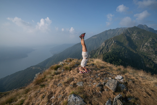 Young woman on mountain top exercising headstand yoga pose on summit after day hike. People travel healthy lifestyle concept