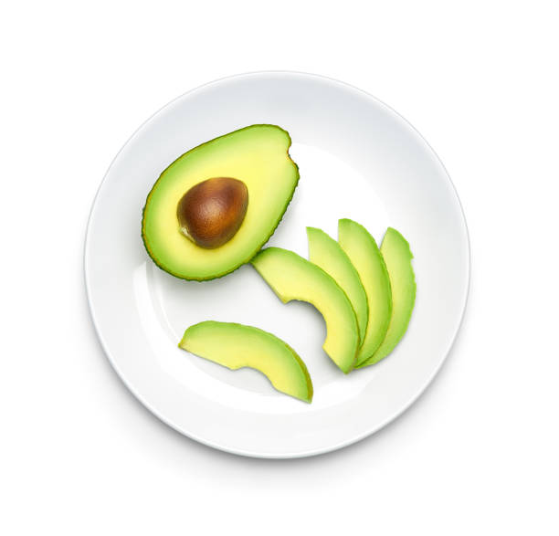 Half and slice avocado on plate over white background, top view stock photo