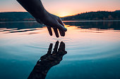 Finger touches surface of mountain lake. Hand reflection