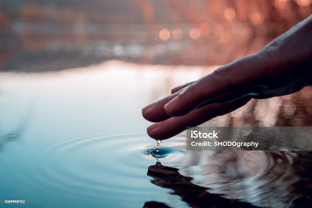 Finger touches surface of mountain lake. Hand reflection reflection on water Water Stock Photo