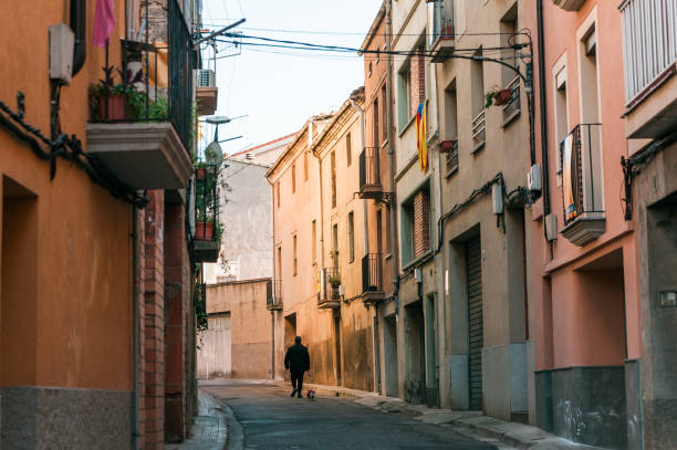 lonely old man with dog walk in street of small catalan spanish medieval town during sunny spring day stock photo