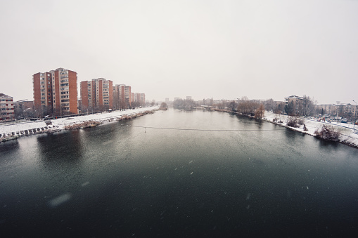 A scenic wide angle view of a flowing river through a Romanian city on an idyllic snowy day.