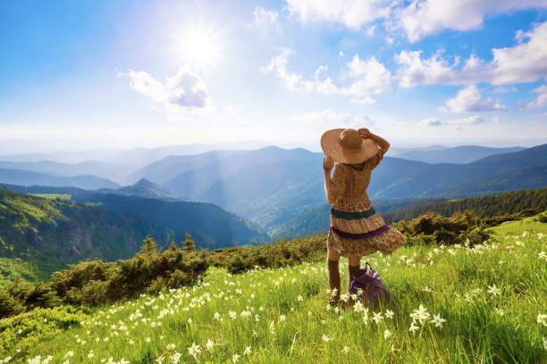 sur la pelouse dans les paysages de montagnes, la fille de hipster en robe, bas et paille chapeau reste regarder le ciel avec des nuages. paysages de printemps magnifique. - spring daffodil flower sky photos et images de collection