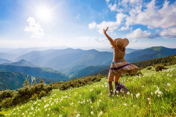 sur la pelouse dans les paysages de montagnes, la fille de hipster en robe, bas et paille chapeau reste regarder le ciel avec des nuages. paysage d’été extraordinaire. belles rayons du soleil. - spring daffodil flower sky photos et images de collection