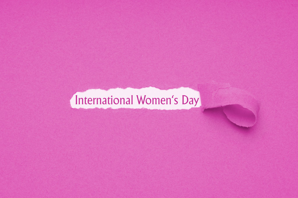 International womens day is celebrated on March 8 - text revealed by hole torn in pink paper background