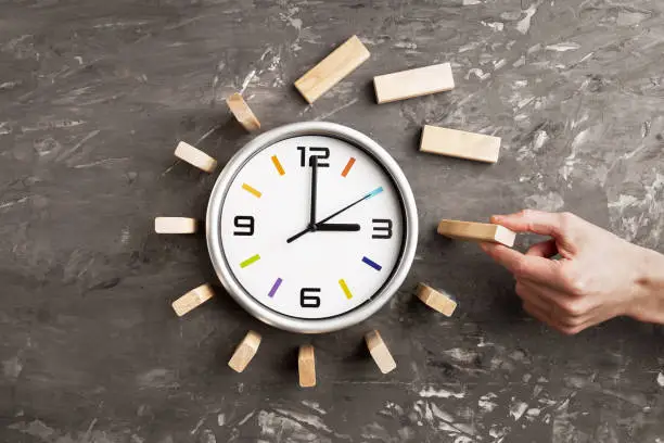 Time management concept. Big clock and wooden cubes, male hand holds a cube. Time comes to an end