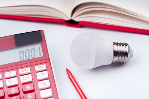 lampadine a risparmio energetico, una calcolatrice e un notebook con penna sono sul tavolo bianco - piggy bank savings pig currency foto e immagini stock