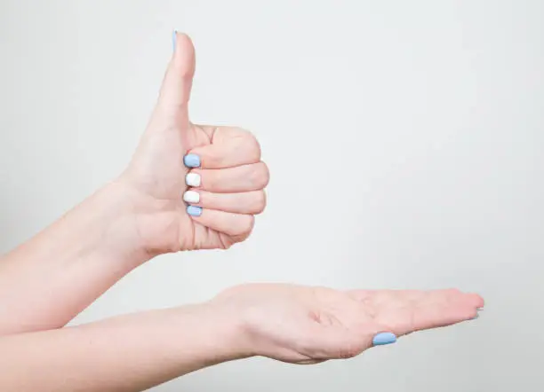 Closeup view of female young hand in likeness gesture with thumb up isolated on white background. Fingernails with white and blue professional modern gel polish.