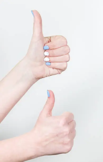 Closeup view of two female hands in likeness gesture with thumb up isolated on white background. Fingernails with white and blue professional modern gel polish.