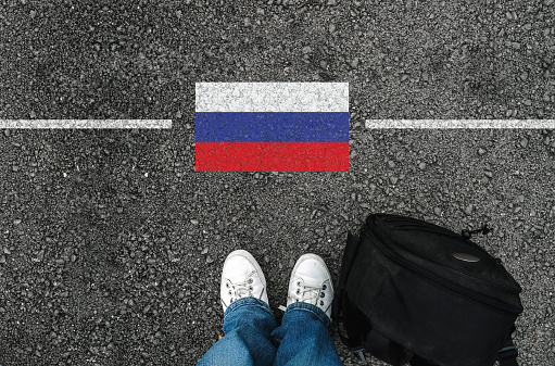 a man with a shoes and backpack is standing on asphalt next to flag of Russia and border