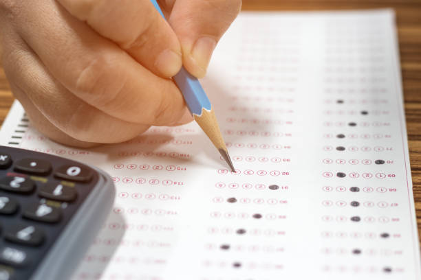 istock Dry hand of mature student doing exams by using pencil selected multiple choice on standardized test form with answers bubble with calculator nearby. Ideas about adult education and life long learning 1090107212