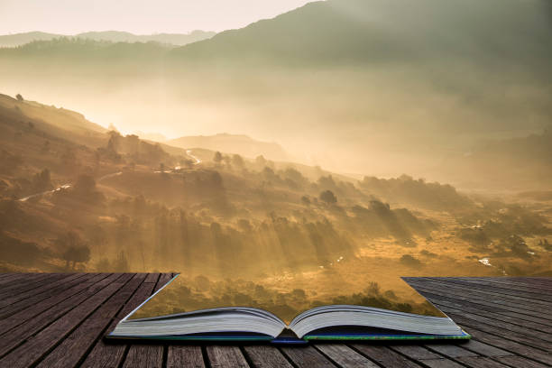 Stunning Autumn Fall landscape sunrise in the Lake District with sun beams streaming through the mist into The Langdales valley coming out of pages of open story book