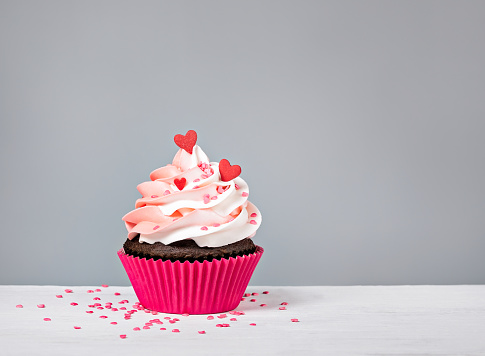 Valentines Day Cupcake treat with buttercream icing and heart sprinkles on a grey background