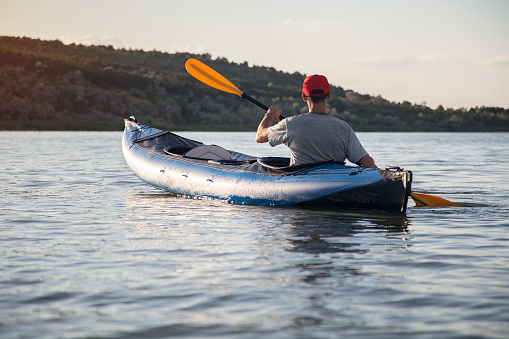 A young man is riding a kayak. Quiet waters and bright sun.