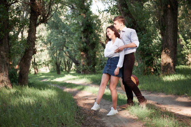 young couple walking in the forest, playing guitar and dancing, summer nature, bright sunlight, shadows and green leaves, romantic feelings