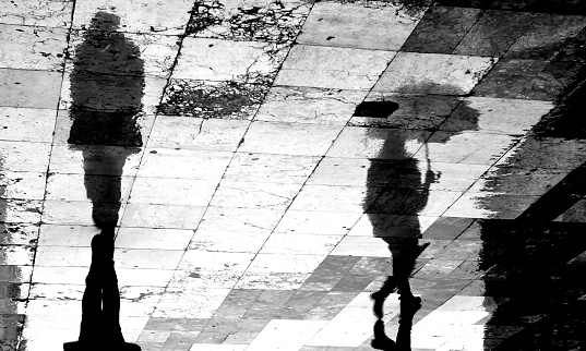 Blurry reflection shadow of two people walking apart the city street patterned sidewalk on a dark rainy day