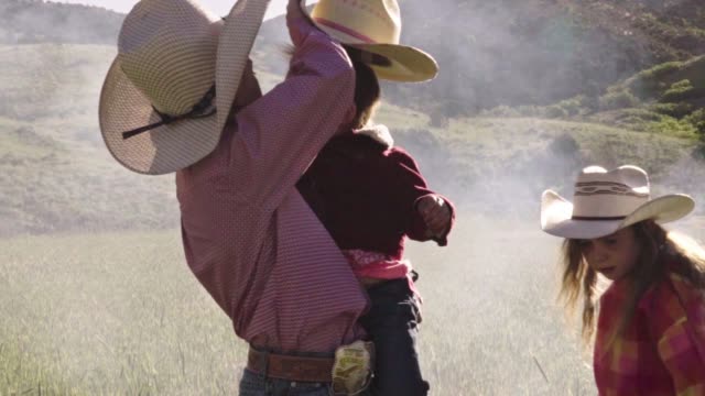 A Young Cowboy Places A Hat On A Little Buckaroo While A Young Girl Watches The Campfire